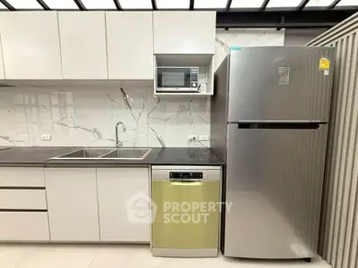 Modern kitchen with sleek cabinetry, stainless steel fridge, and built-in microwave.