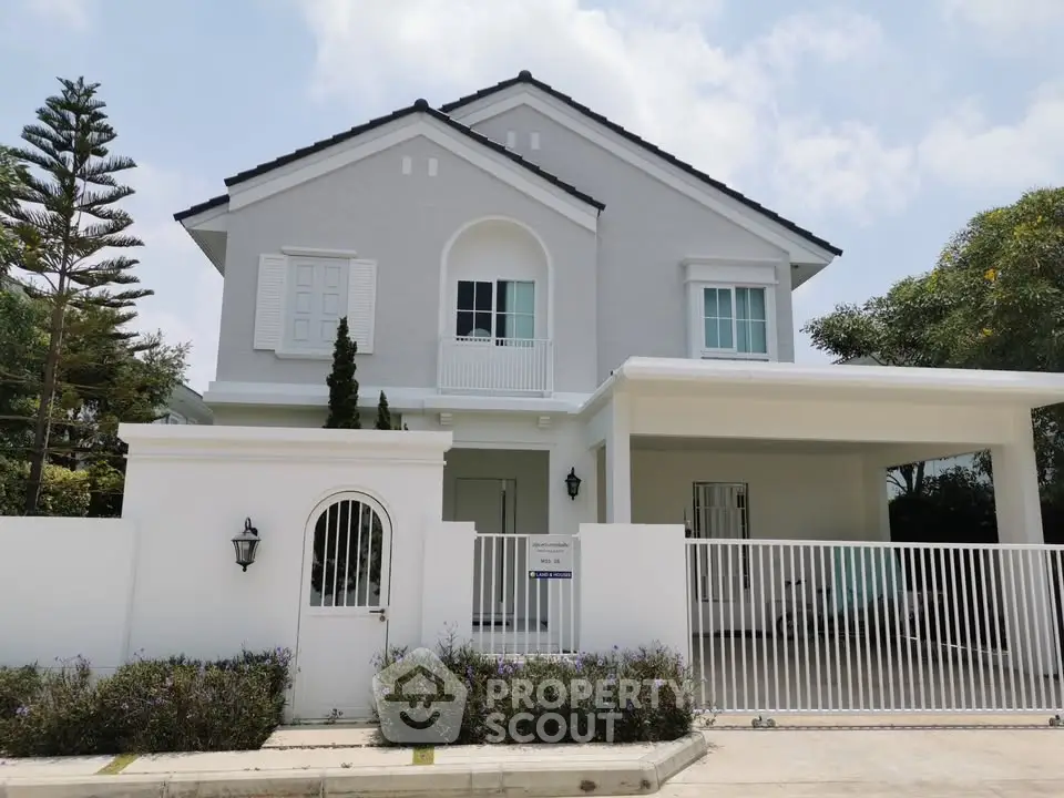 Elegant two-story white house with gated entrance and lush greenery
