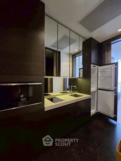 Modern kitchen with sleek dark cabinetry and built-in appliances, featuring an open fridge and stylish design.