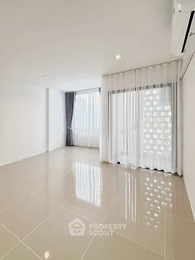 Spacious unfurnished living room with large windows and elegant curtains.