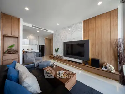 Modern living room with sleek design, featuring a large TV, wooden accents, and open kitchen layout.