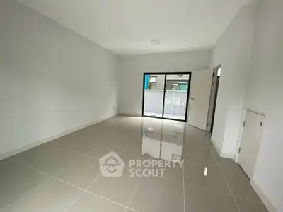 Spacious empty room with glossy tiled floor and sliding glass door leading to balcony.