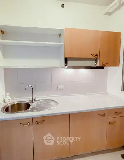 Compact kitchen with wooden cabinets and stainless steel sink in modern apartment.