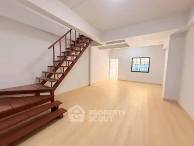 Spacious open-plan room with wooden staircase and bright natural light.