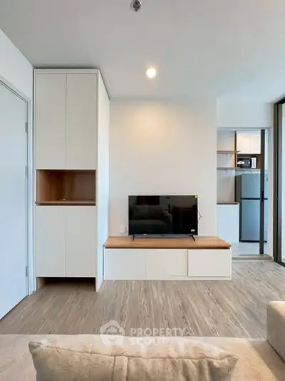 Modern living room with sleek TV setup and open kitchen view, featuring contemporary design and ample natural light.