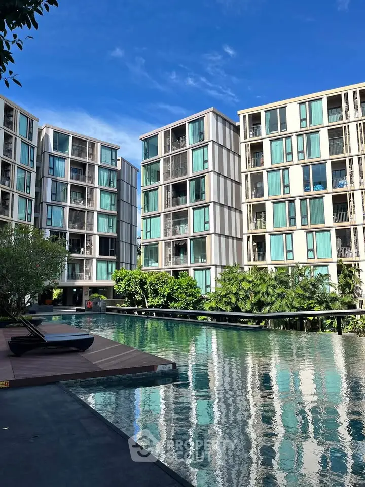 Modern apartment complex with stunning pool and lush greenery under clear blue sky.