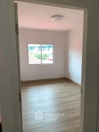Bright empty room with wooden flooring and large window offering natural light.