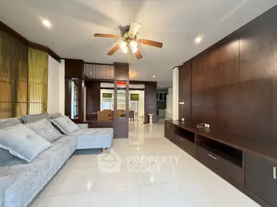 Spacious living room with modern design and ceiling fan, featuring elegant wooden accents and plush seating.