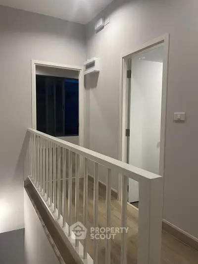 Modern interior hallway with wooden flooring and white railing, leading to closed doors.