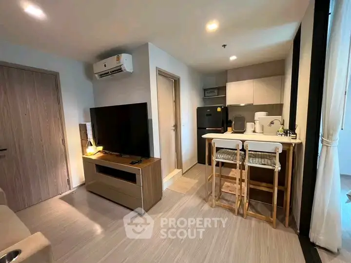 Modern open-plan living room with kitchen, featuring sleek furniture and natural lighting.