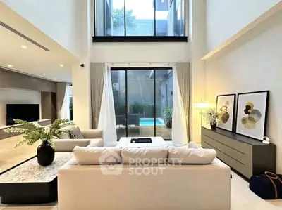 Luxurious modern living room with high ceilings and pool view, featuring elegant decor and natural light.