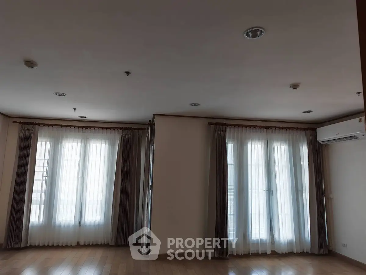 Spacious living room with large windows and elegant curtains, featuring wooden flooring and modern lighting.