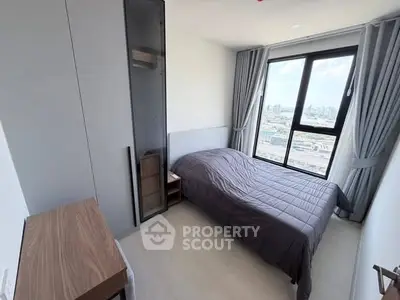 Modern bedroom with city view, featuring sleek furniture and large window for natural light.