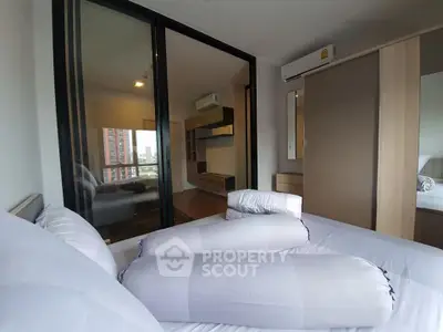 Modern bedroom with sliding glass doors and city view, featuring stylish furniture and air conditioning.