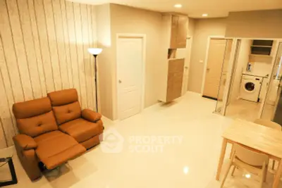 Modern living room with cozy recliner and open kitchen layout featuring a washing machine.