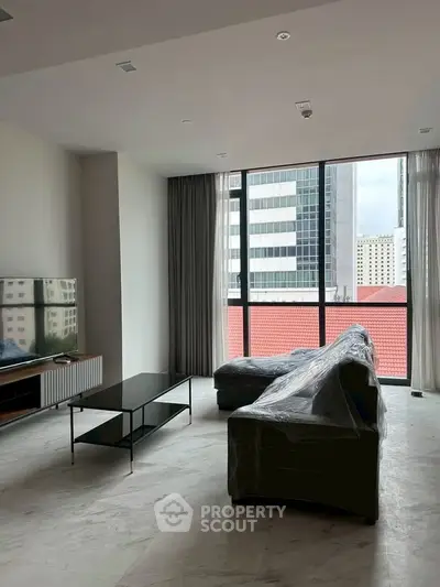 Spacious modern living room with large windows and city view, featuring sleek furniture and natural light.