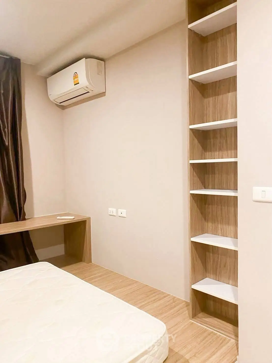 Modern bedroom with built-in shelves and air conditioning, featuring minimalist design and neutral tones.