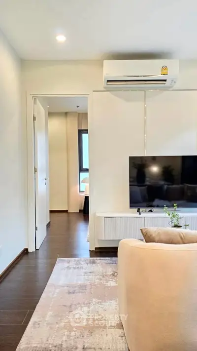 Modern living room with sleek design, featuring a wall-mounted TV and air conditioning, leading to a cozy bedroom.