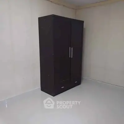 Minimalist room with a sleek dark wardrobe against a plain wall.
