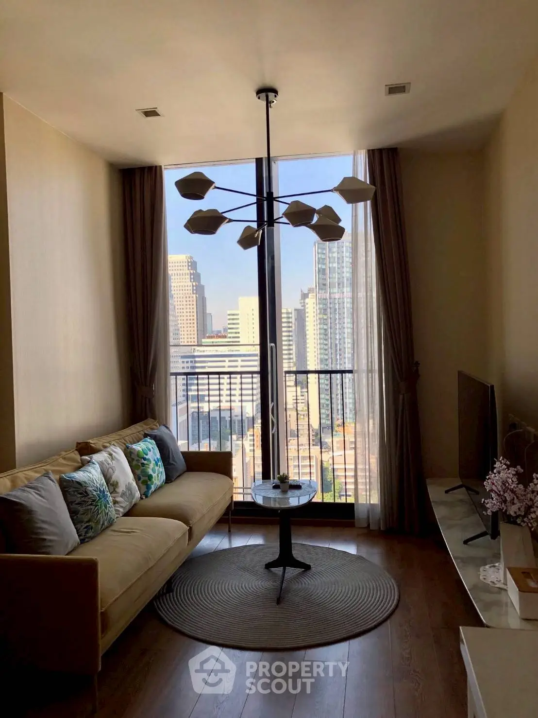 Modern living room with city view, stylish chandelier, and cozy sofa in high-rise apartment.