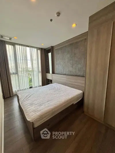 Modern bedroom with large window and wooden flooring in a stylish apartment.