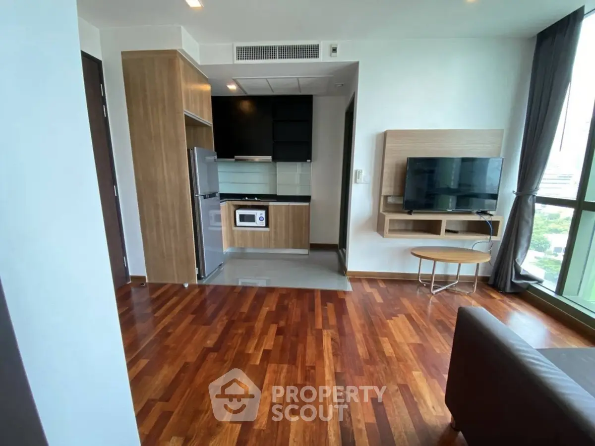 Modern living room with open kitchen and wooden flooring in high-rise apartment.