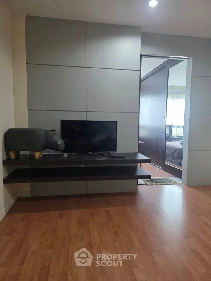 Modern living room with sleek TV setup and wooden flooring, adjacent to a cozy bedroom.