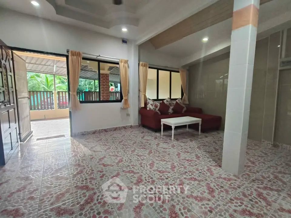 Spacious living room with tiled floor and cozy red sofa, featuring large windows and natural light.