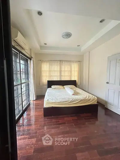 Spacious bedroom with wooden flooring and natural light