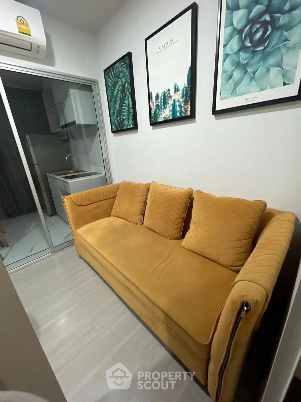 Cozy living room with mustard sofa and modern decor, adjacent to a compact kitchen area.