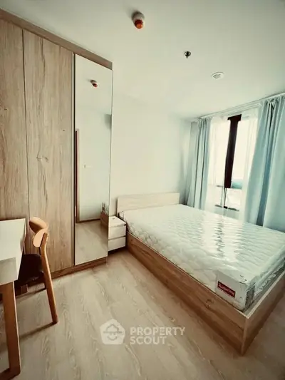 Modern bedroom with wooden furniture and large window offering natural light.