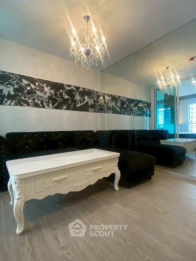 Luxurious living room with elegant chandelier and mirrored wall, featuring a stylish black sofa and chic white coffee table.
