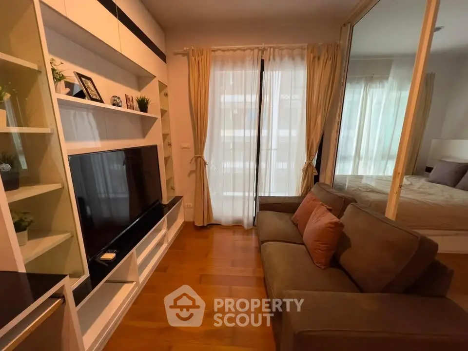 Cozy living room with modern decor and large TV, adjacent to a bedroom with glass partition.