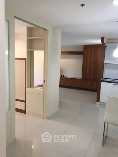 Modern apartment interior with sleek kitchen and open layout, featuring white tiles and wooden cabinetry.