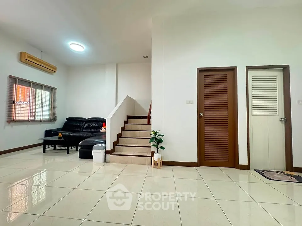 Spacious living room with modern staircase and sleek black sofa, perfect for family gatherings.