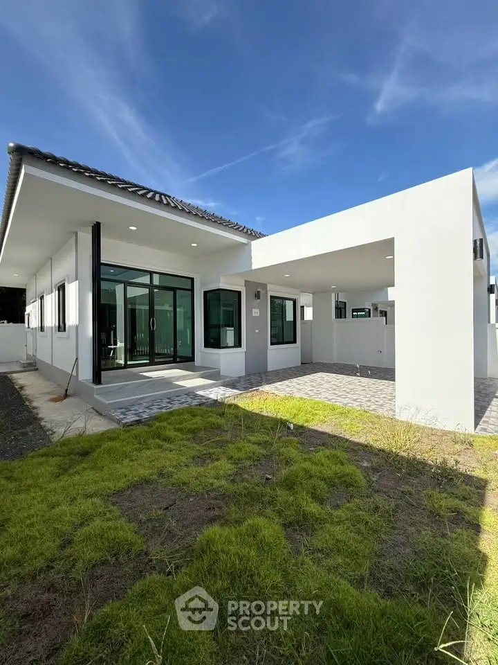 Modern single-story house with large windows and spacious front yard under clear blue sky.