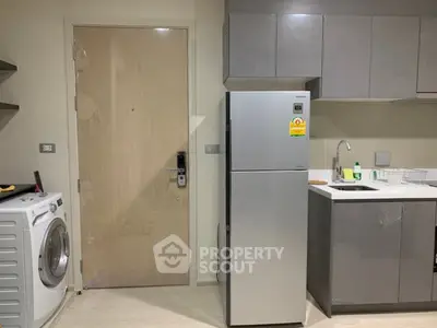 Modern kitchen with sleek cabinetry, stainless steel fridge, and washing machine in compact apartment.