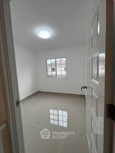 Spacious empty room with tiled flooring and natural light from window.