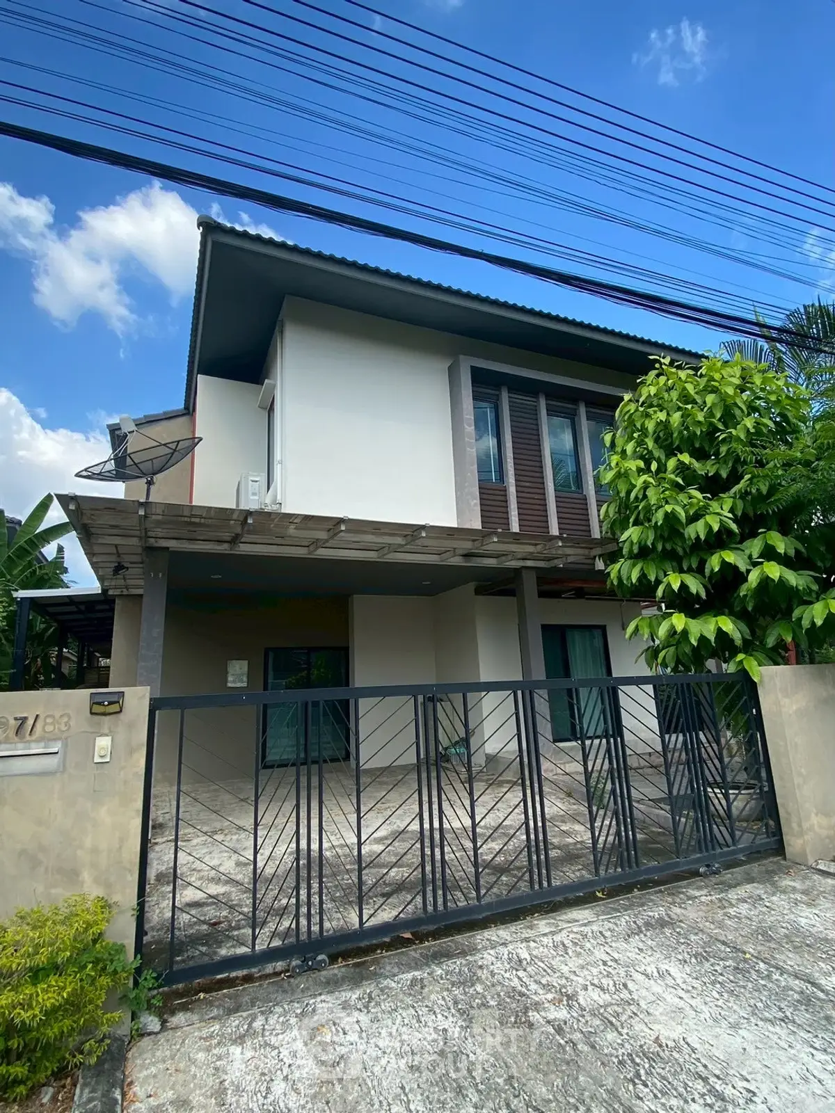 Modern two-story house with gated driveway and lush greenery, perfect for family living.