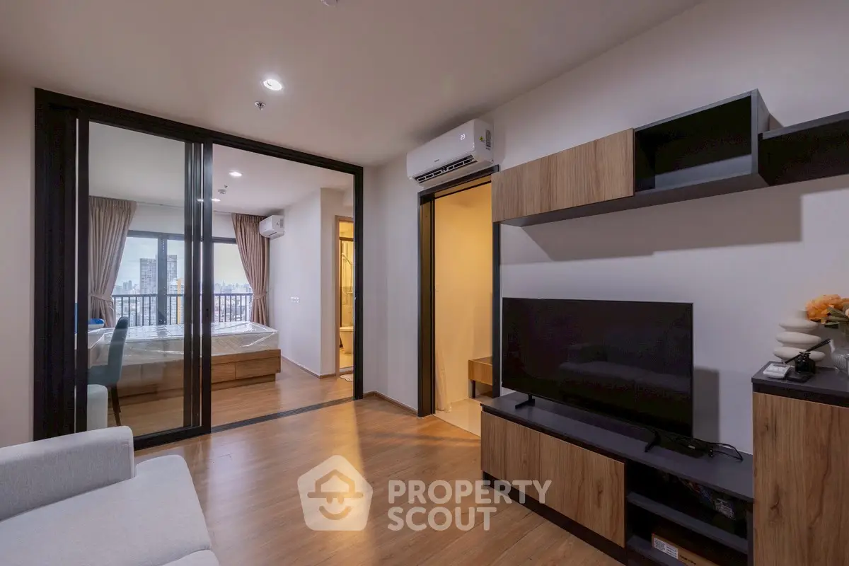 Modern living room with wooden flooring and sleek furniture, featuring a view into a cozy bedroom.