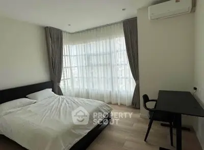 Modern bedroom with large windows and natural light, featuring a bed and study desk.