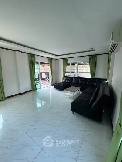 Spacious living room with modern black leather sofa and green curtains, perfect for relaxation.