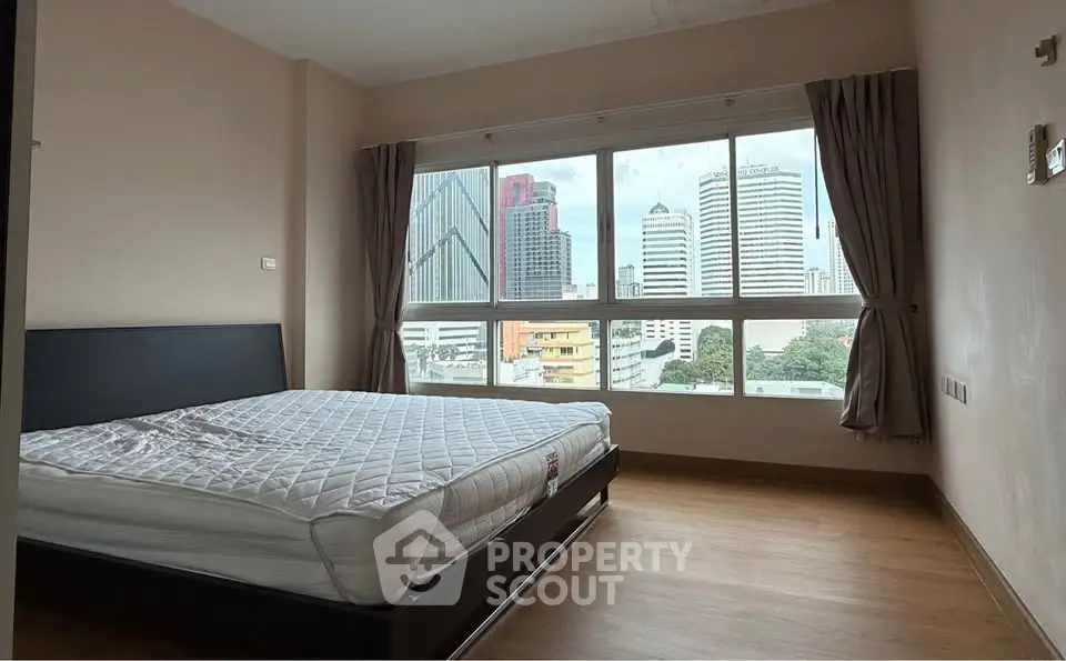 Spacious bedroom with city view and large windows in modern apartment.