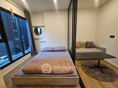 Modern bedroom with cozy seating area and large windows in urban apartment.