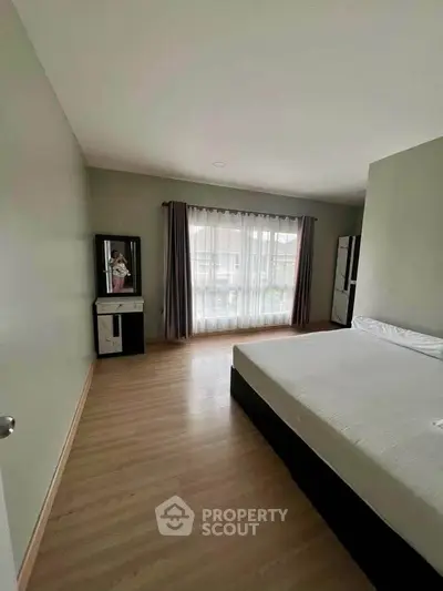 Spacious bedroom with large window and minimalist decor, perfect for relaxation and comfort.