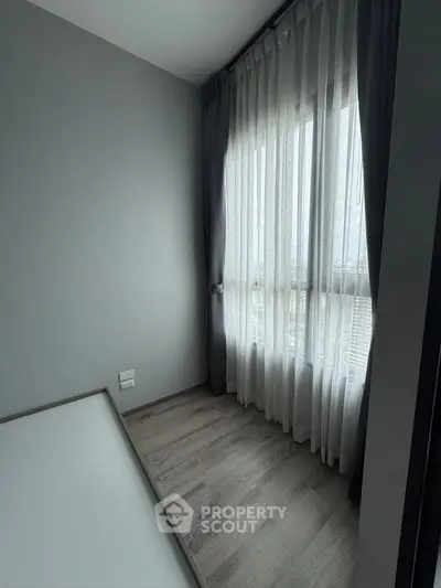 Minimalist bedroom with large window and sheer curtains, offering ample natural light and a serene atmosphere.