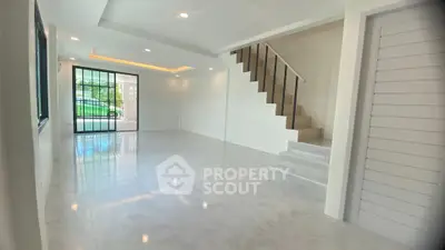 Spacious modern living room with elegant staircase and large windows for natural light.