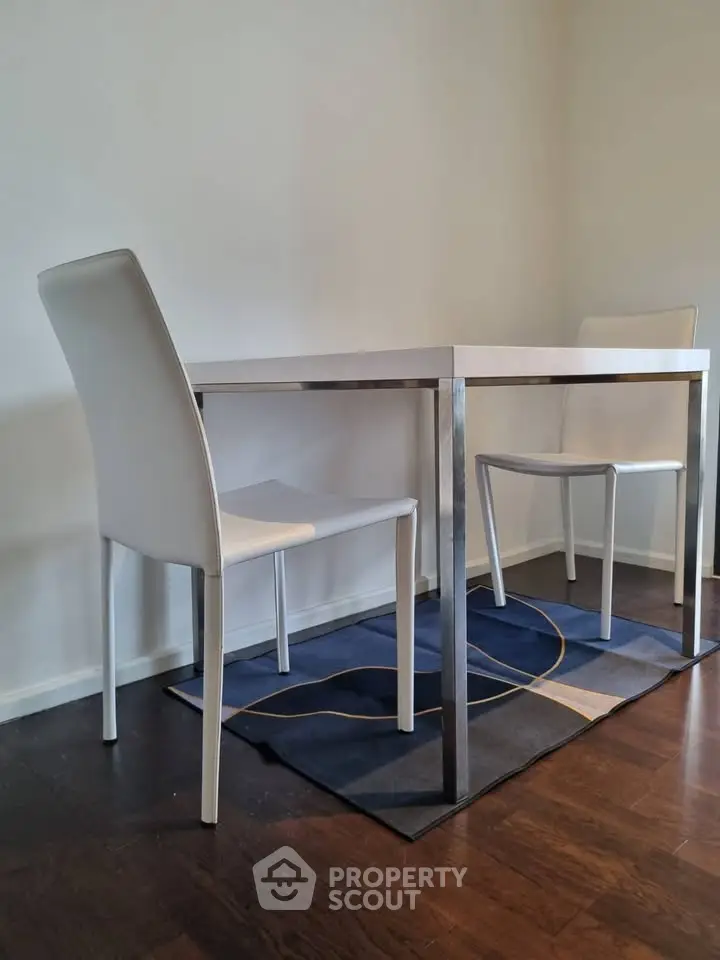 Modern dining area with sleek white chairs and minimalist table on dark wood floor.