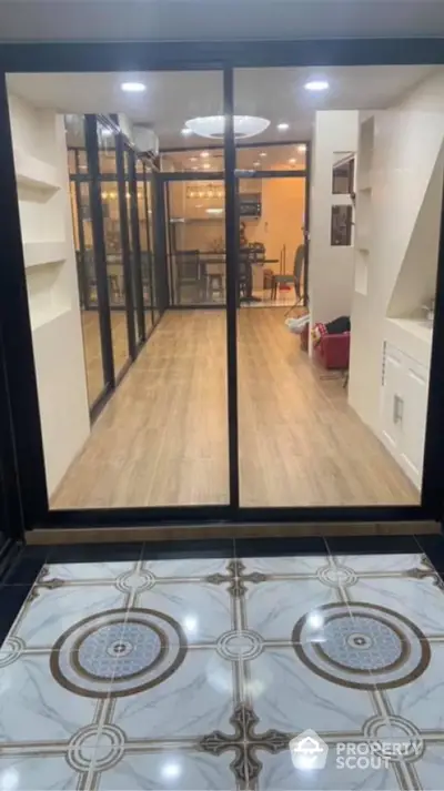 Elegant home interior featuring glossy marble flooring at the entrance and warm wooden floors in a spacious living area with modern glass partition doors.