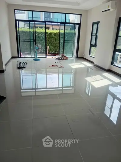 Spacious living room with large windows and glossy tiled floor, offering abundant natural light and garden view.